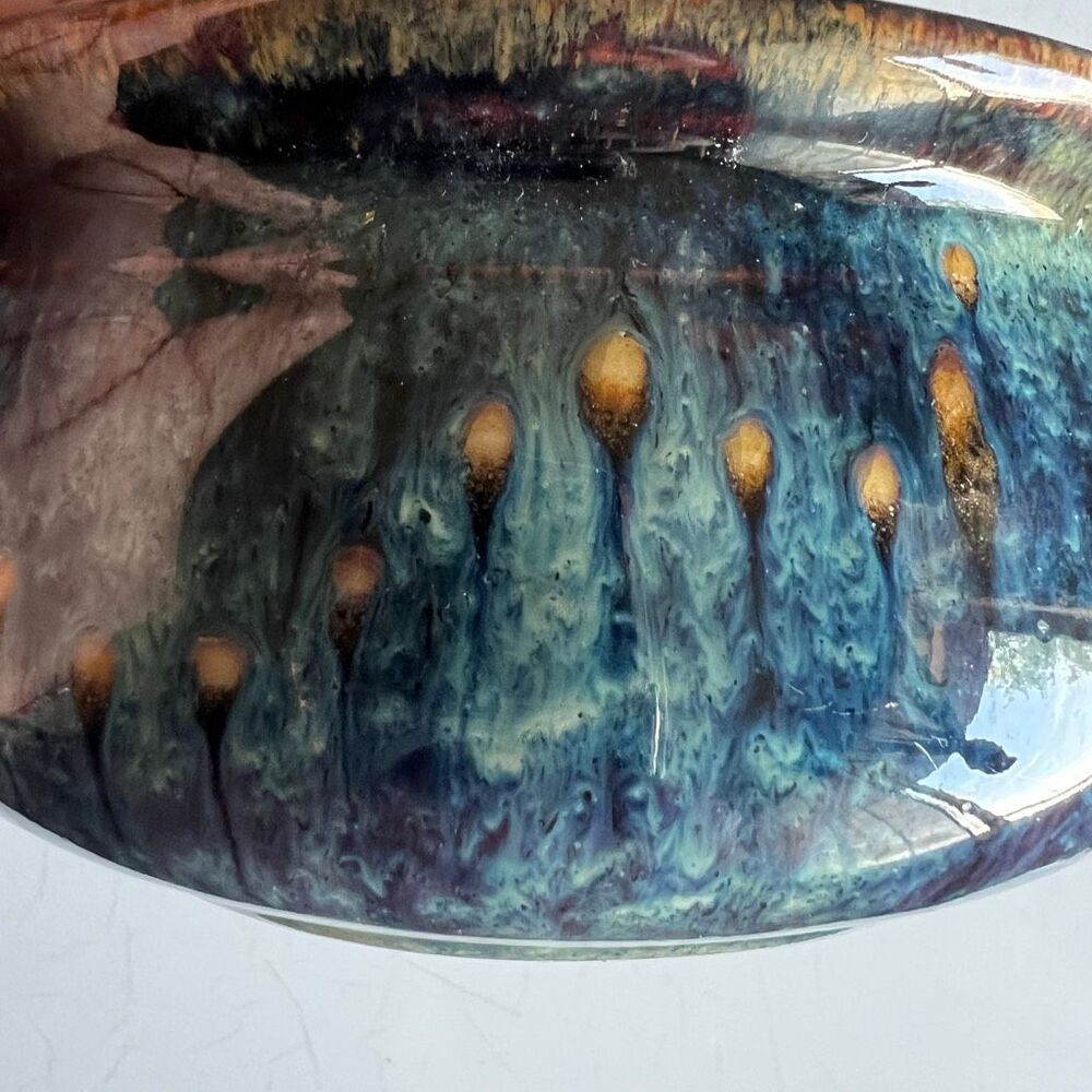 This pottery bowl features a complex glaze with drips of blue, purple, and bronz